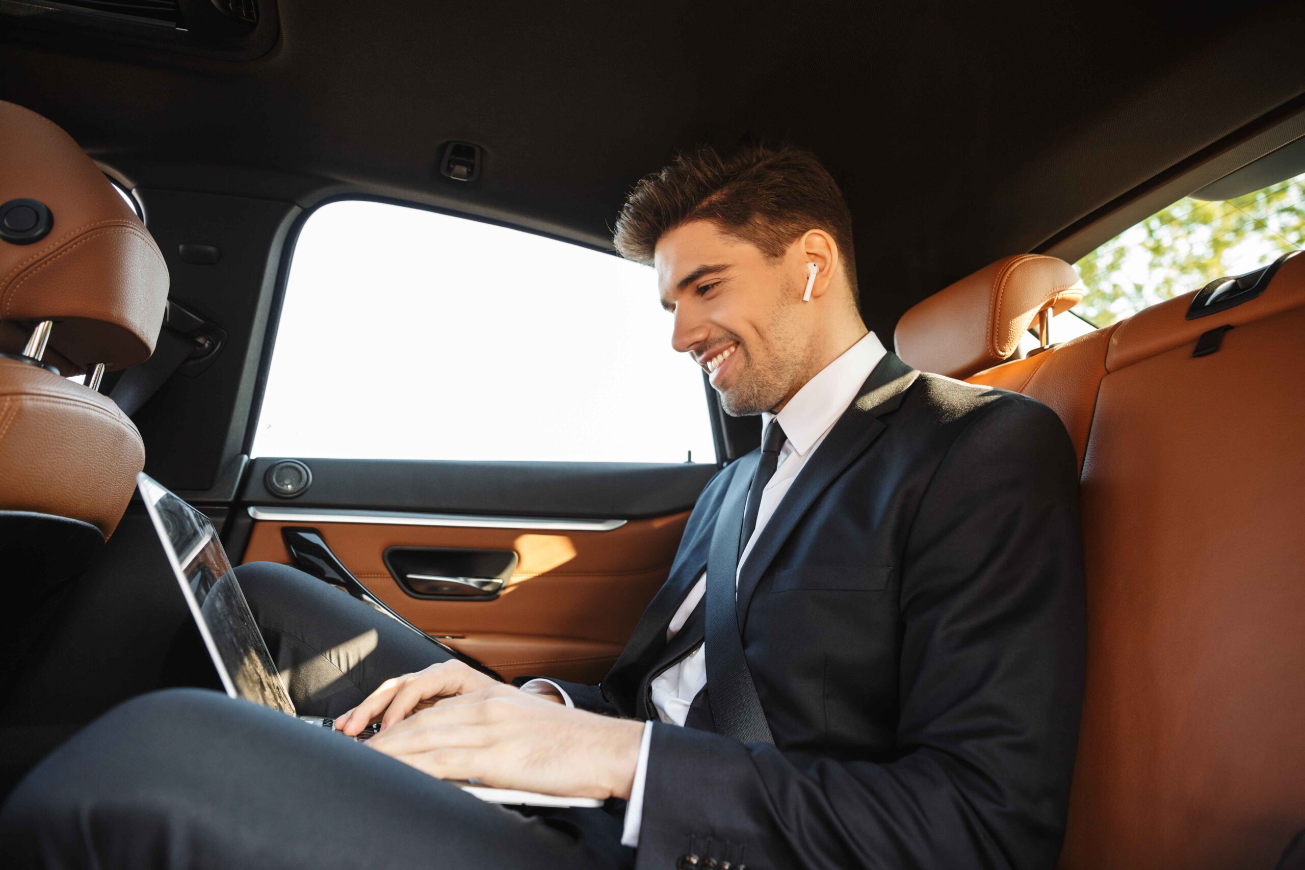 smiling-young-businessman-formal-wear-using-earpod-laptop-while-going-car (1)